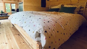 A wooden cabin bedroom with a bed, a hanging light fixture, and a window. - B&B Voor De Wind (Slootdorp)
