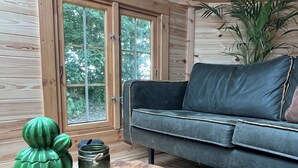 A wooden interior with a sofa, a round wooden table, and a large window. - B&B Voor De Wind (Slootdorp)