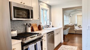 A modern kitchen with white cabinetry, stainless steel appliances, and a patterned rug. - Charming Cape Cod Getaway- EV Charger, Mini Golf, Walk to The Beach, Pets Okay! (Yarmouth)