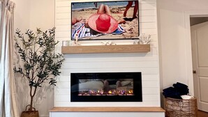 A living room with a flat-screen TV mounted on a white wall above a fireplace. - Charming Cape Cod Getaway- EV Charger, Mini Golf, Walk to The Beach, Pets Okay! (Yarmouth)
