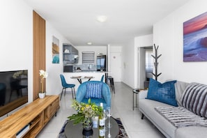 A modern living room with a sofa, a coffee table with a vase and wine glasses, a wooden bench, and a TV.