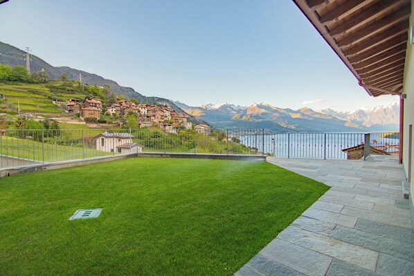 Eine Terrasse mit Blick auf einen See und Berge, eine Rasenfläche und ein Kiesweg.