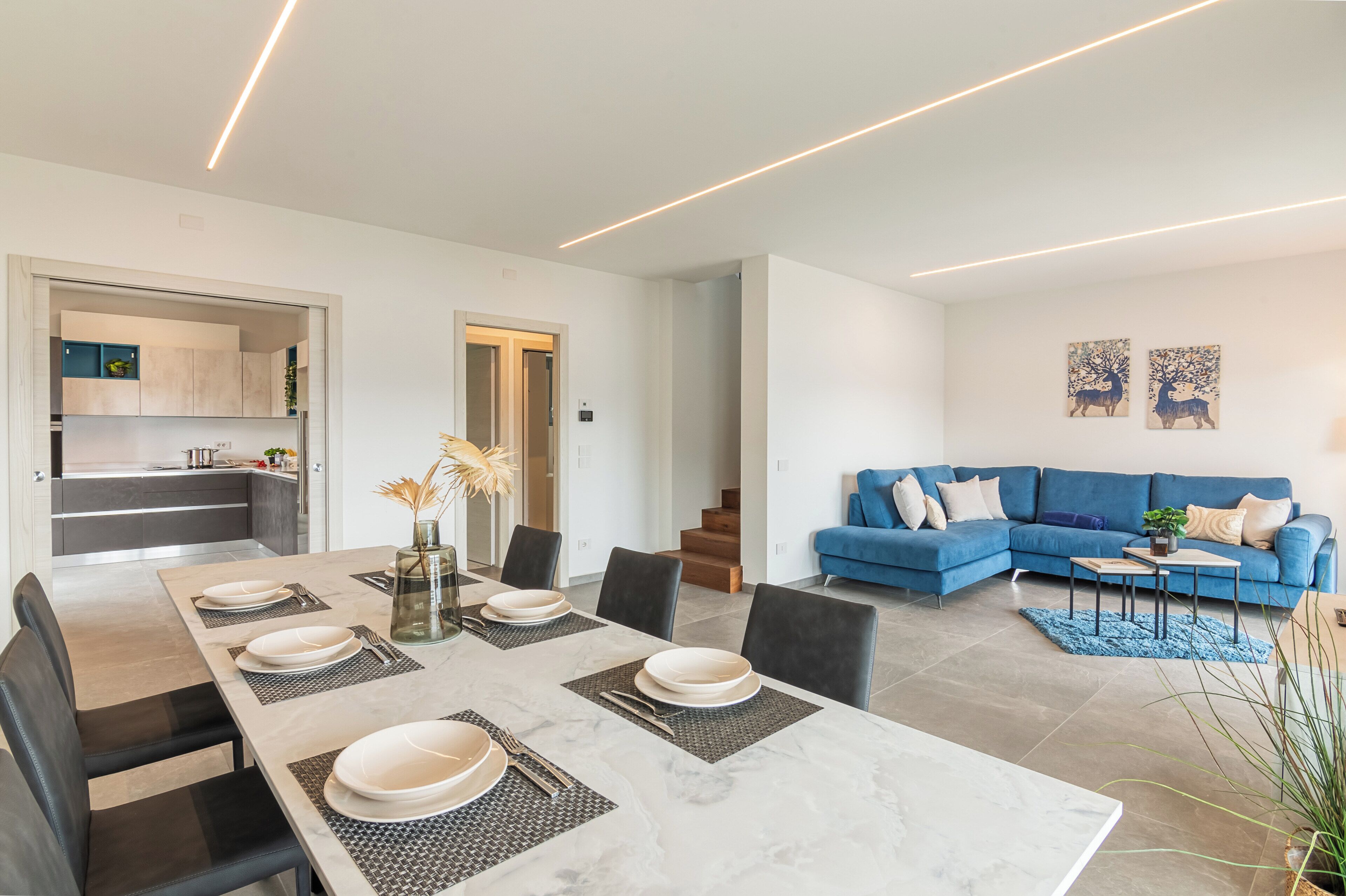 Ein modernes Wohnzimmer mit einem blauen Sofa, einem Esstisch für vier Personen und einer Küche im Hintergrund.