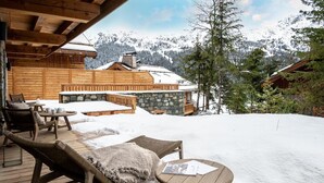 A wooden deck with outdoor seating, a stone wall, and a view of snow-covered mountains. - Wifi, 150m from ski slopes, Ground floor, sauna, hammam, terrace, fireplace or stove, tv, 120m² (Méribel - Les Allues)