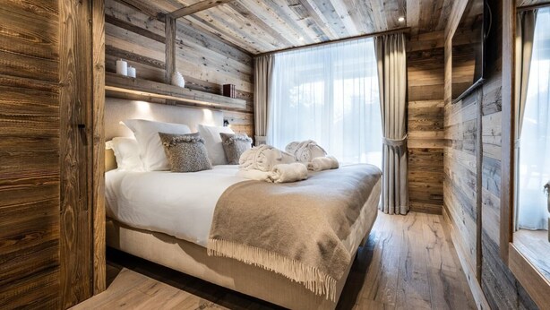 A wooden cabin bedroom with a bed, pillows, and a blanket. - Wifi, 150m from ski slopes, Ground floor, sauna, hammam, terrace, fireplace or stove, tv, 120m² (Méribel - Les Allues)