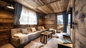 Accogliente interno di una baita in legno, con un divano, un tavolo di legno e vista sull'esterno.