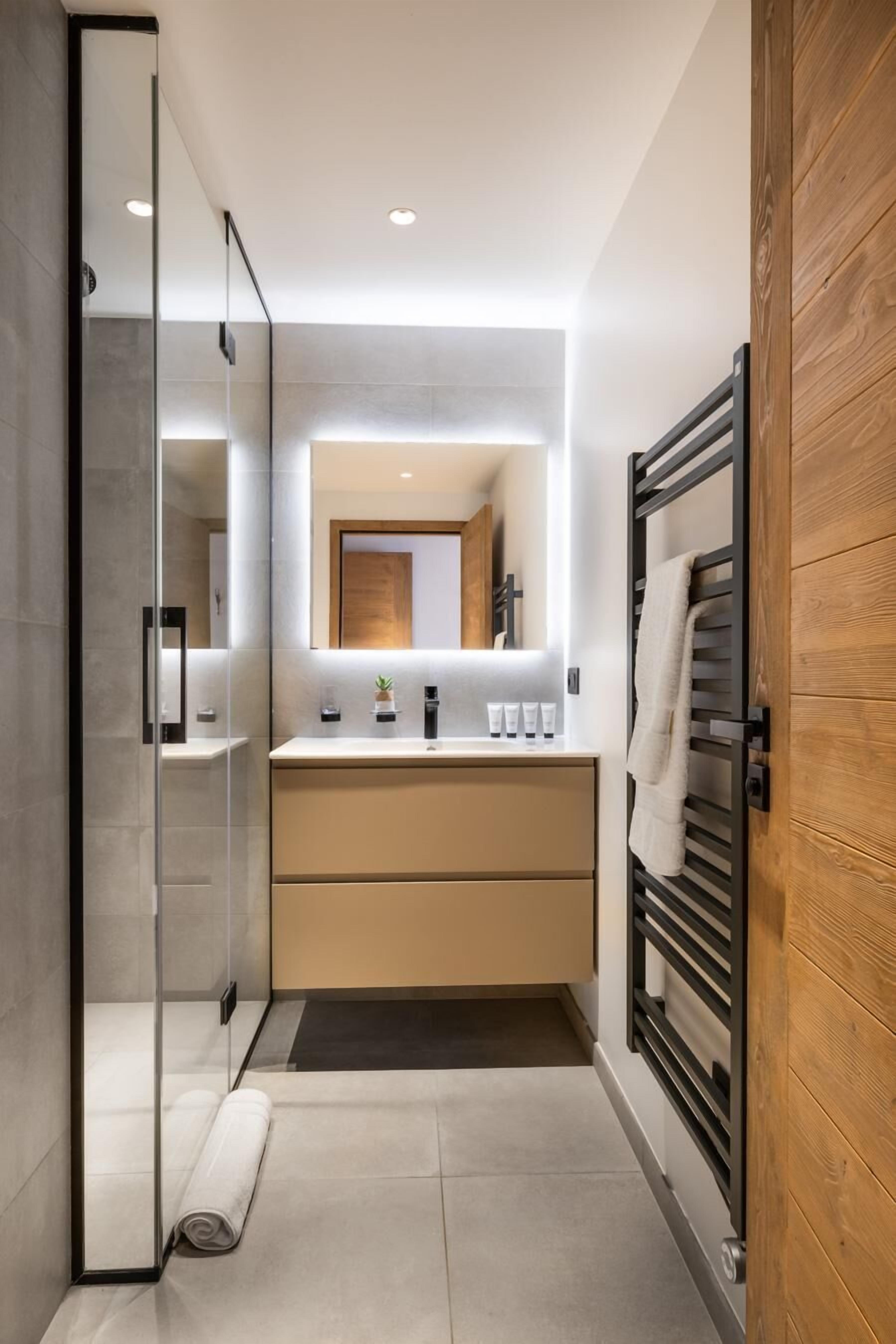 A modern bathroom with a glass shower enclosure, a wooden vanity, and a towel rack.