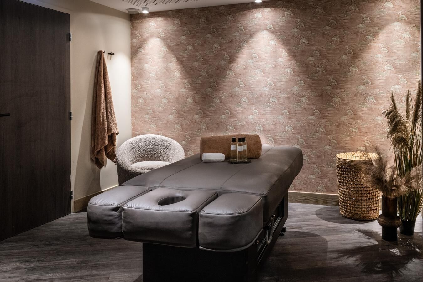 Un cuarto de masajes con una camilla, una silla y un decorado de pared con diseño de hojas.