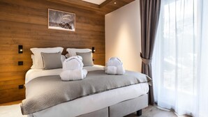 A modern hotel room with a wooden headboard, a large bed with a grey blanket, two white towels, and a framed picture above the bed. - Wifi, 150m from ski slopes, Ground floor, sauna, hammam, terrace, fireplace or stove, tv, 136m² (Méribel - Les Allues)