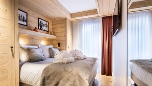 A cozy wooden room with a bed, a shelf with framed photos, and a window with curtains. - Wifi, 150m from ski slopes, view mountain, sauna, hammam, terrace, balcony, tv, 78m², Méribel (Méribel - Les Allues)