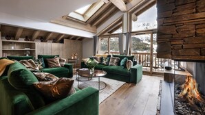 A modern living room with green sofas, a fireplace, and large windows offering a view of the outdoors. - Wifi, 150m from ski slopes, 1st floor, view mountain, sauna, hammam, terrace, balcony (Méribel - Les Allues)