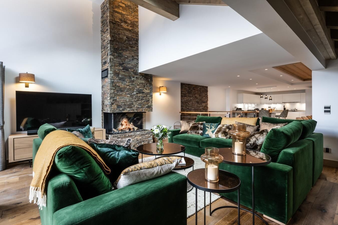 Ein modernes Wohnzimmer mit Kamin aus Stein, grünen Sofas und einem Flachbildfernseher.