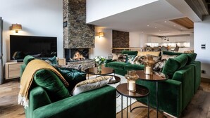 A modern living room with a stone fireplace, green sofas, and a flat-screen TV. - Wifi, 150m from ski slopes, 1st floor, view mountain, sauna, hammam, terrace, balcony (Méribel - Les Allues)