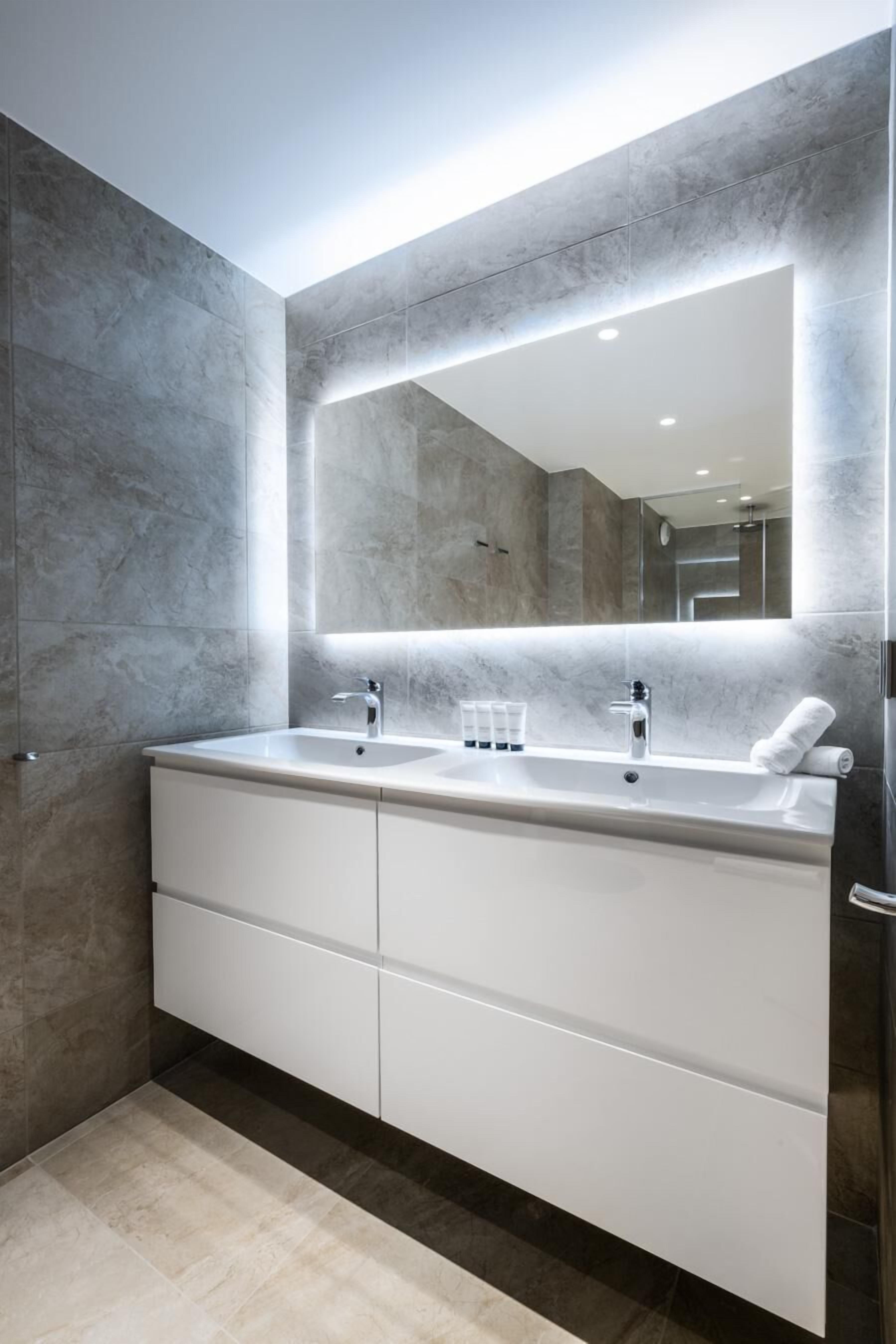 Une salle de bain moderne avec un grand miroir, deux vasques et un meuble-lavabo blanc.