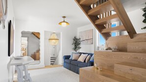 A modern living room with a staircase, a blue sofa, a white table, and a hanging light fixture. - West of Town, a quiet corner of luxury  (Nantucket)