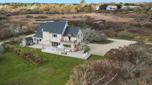 A large house with a spacious deck, a well-maintained lawn, and a view of the surrounding landscape. - West of Town, a quiet corner of luxury  (Nantucket)