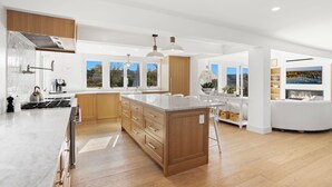 A spacious kitchen with wooden cabinets, a large island, and a modern pendant light. - West of Town, a quiet corner of luxury  (Nantucket)
