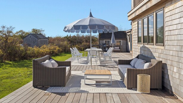 An outdoor patio with wicker furniture, a table, and a large umbrella. - West of Town, a quiet corner of luxury  (Nantucket)