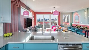 A modern kitchen with a large island, a dining area with blue chairs, and a city view through large windows. - Pink Palace ⁞ DT views ⁞ 5min 2 Broadway (Nashville)