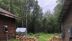 A wooden cabin with a gravel pathway leading to a shed, surrounded by a forest. - Quaint Rural Cabin Near Hatcher Pass (Wasilla)