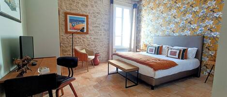 A bedroom with a bed, a desk, a chair, and a painting on the wall.