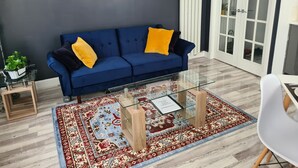A modern living room with a blue sofa, glass coffee table, and a patterned rug. - Charming Ab25 Free Parking (Aberdeen)