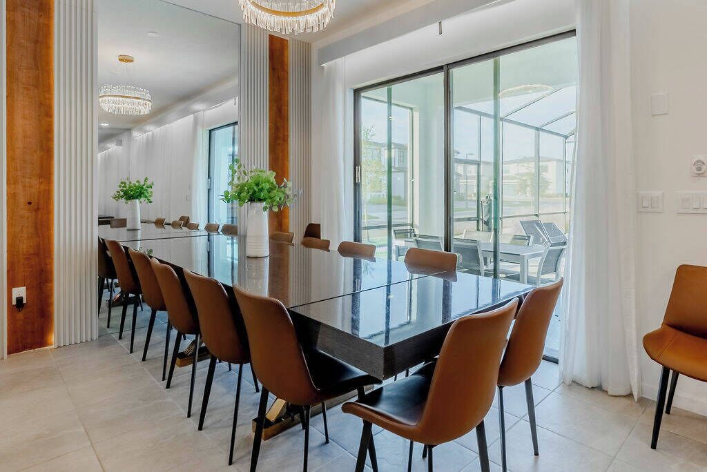 A modern dining area with a glass table, brown chairs, and a large window offering a view of the outdoors.