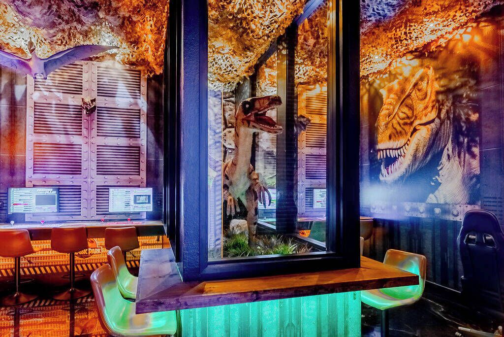 Una habitación con un recinto de cristal que exhibe un esqueleto de dinosaurio, una mesa de madera y sillas.
