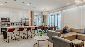 A modern kitchen with stainless steel appliances, a dining area with red chairs, and a large window providing natural light.