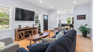 Una sala de estar moderna con un televisor grande, un mueble de entretenimiento de madera y un rincón de estar acogedor.