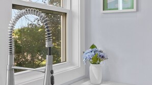 Una cocina moderna con un lavamanos de acero inoxidable, un ventanal con vistas a árboles y un cuadro en la pared.