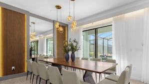 A modern dining area with a long wooden table, beige chairs, and hanging spherical light fixtures.