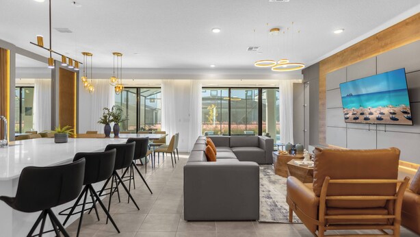 A modern living room with a grey sectional sofa, a wooden chair, and a dining area with black chairs and a white table.