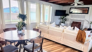 A living room with a sofa, a dining table with chairs, a TV mounted on the wall, and a fireplace. - Surf & Sand, MCM Coastal Escape, Pet-friendly (Crescent City)