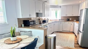 A modern kitchen with white cabinets, a stainless steel refrigerator, and a built-in microwave. - Surf & Sand, MCM Coastal Escape, Pet-friendly (Crescent City)