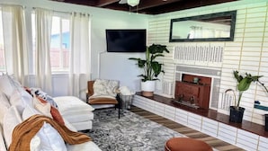 A living room with a sofa, a chair, a coffee table, a fireplace, and a TV mounted on the wall. - Surf & Sand, MCM Coastal Escape, Pet-friendly (Crescent City)