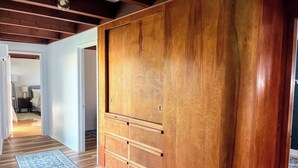 A hallway with wooden flooring, a blue patterned rug, and a wooden wardrobe with drawers. - Surf & Sand, MCM Coastal Escape, Pet-friendly (Crescent City)