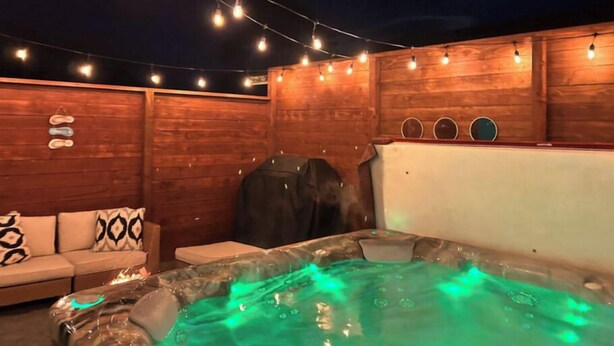 A hot tub with green lighting, a wooden wall, and string lights. - Surf & Sand, MCM Coastal Escape, Pet-friendly (Crescent City)