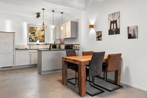 A modern kitchen with white cabinetry, a wooden dining table, and pendant lighting.