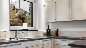 Eine moderne Küche mit hellen Schränken, einem großen Fenster mit Blick auf Felsen und einer schwarzen Kaffeemaschine.