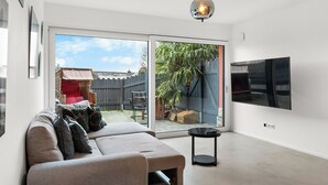 Ein modernes Wohnzimmer mit einer Couch, einem Fernseher und einer Schiebetür, die in einen Garten führt.