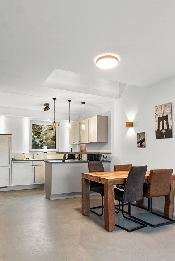 A modern kitchen with white cabinets, a wooden dining table, and pendant lighting.