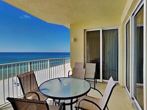A balcony with a glass table and chairs, overlooking a beach and the ocean. - Boardwalk #1008 by Resort Collection (Panama City Beach)