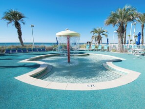 A pool area with a water feature, lounge chairs, and palm trees. - Boardwalk #1008 by Resort Collection (Panama City Beach)