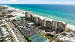 A beachfront hotel with multiple buildings, a parking lot, and a tennis court. - Moonspinner 415A by Resort Collection (Panama City Beach)