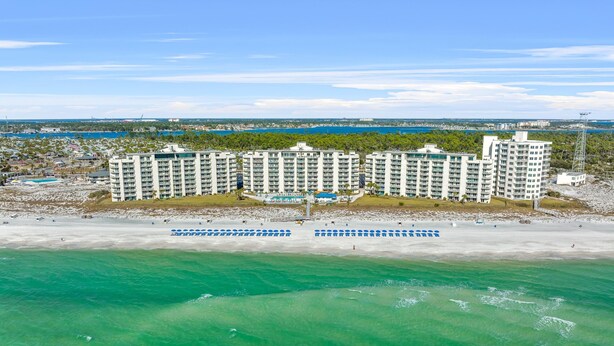 A beachfront hotel with multiple high-rise buildings, a pool area, and a beach with umbrellas. - Moonspinner 415A by Resort Collection (Panama City Beach)