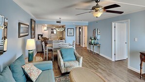 A living room with a sofa, chairs, a dining area, and a kitchen in the background. - Moonspinner 415A by Resort Collection (Panama City Beach)