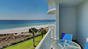 A balcony with a glass table and chairs, overlooking a beach with a clear view of the ocean. - Moonspinner 415A by Resort Collection (Panama City Beach)