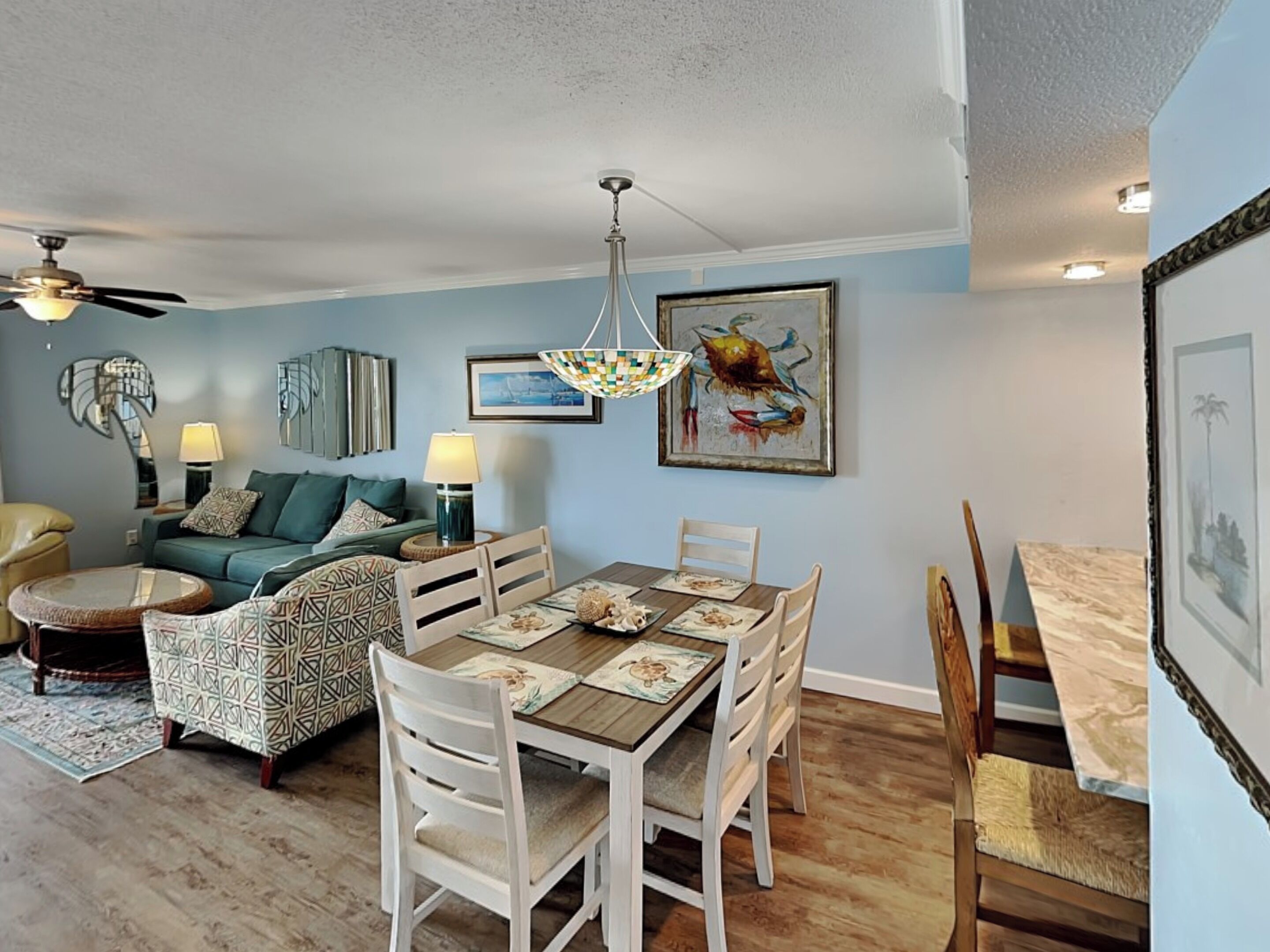 A dining area with a wooden table and white chairs, a sofa, and a ceiling fan.
