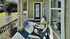 A covered porch with two Adirondack chairs, a white picket fence, and a door with frosted glass panels. - Paradise Escape by Southern Vacation Rentals (Destin)
